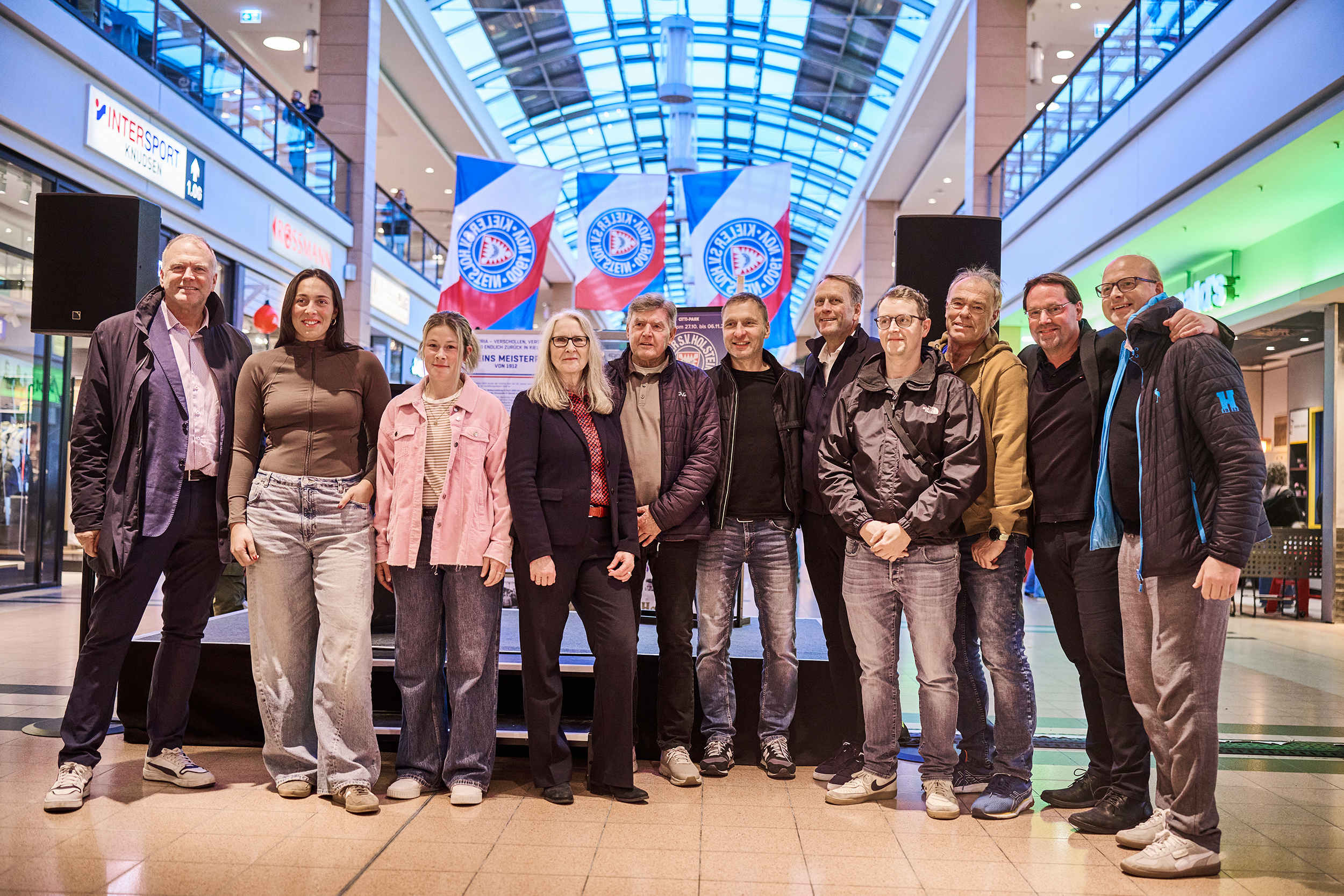 Club Historiker Patrick Nawe mit Geschäftsführer Wolfgang Schwenke, den Holstein Women Spielerinnen Lela Naward Sarah Begunk, der Citti-Park-Kiel-Centermanagerin Silke Brombacher, den Legenden Harry Witt und Daniel Jurgeleit, dem Präsidenten Steffen Schneekloth und der Legende Immo Stelzer